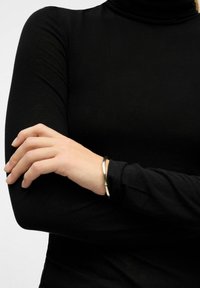 Crni dukserica dugih rukava s uskim teksturama; zapešće ukrašeno tankim crnim i srebrnim narukvicama s elegantnim kružnim dizajnom.