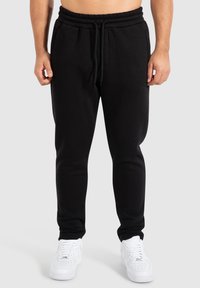 Schwarze Baumwoll-Sweatpants mit verstellbarem Bund und Bündchen, ausgestattet mit zwei Seitentaschen und einem dezenten Logodetail an der Hüfte.