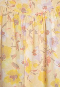 Ύφασμα με λουλουδάτο σχέδιο σε απαλό κίτρινο χρώμα, με ροζ, μωβ και πορτοκαλί λουλούδια· ελαφρύ, υφασμάτινο πλέγμα με πτυχές.