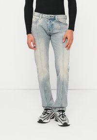 Τζιν ίσια γραμμή σε ανοιχτό γαλάζιο χρώμα με ξεβάμματα, πέντε τσέπες και αντίθετη ραφή; συνδυασμένα με μαύρο μακρυμάνικο τοπ και αθλητικά παπούτσια.