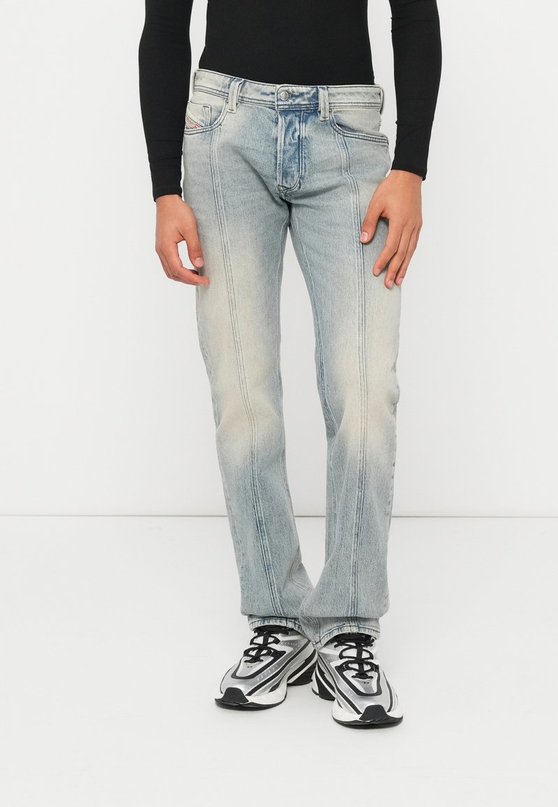 Τζιν ίσια γραμμή σε ανοιχτό γαλάζιο χρώμα με ξεβάμματα, πέντε τσέπες και αντίθετη ραφή; συνδυασμένα με μαύρο μακρυμάνικο τοπ και αθλητικά παπούτσια.