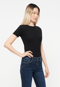 Black short-sleeve fitted top made of ribbed fabric, paired with dark blue jeans featuring a button and zipper closure.