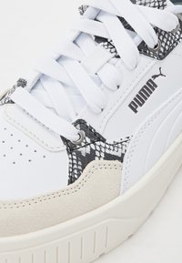 Baskets blanches avec des accents en imprimé serpent gris texturé, des matériaux en cuir lisse et en daim, et des lacets plats blancs. Logo mat sur le côté.