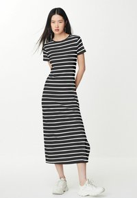 Robe maxi à rayures noires et blanches avec un col rond et des manches courtes, associée à des baskets blanches sur un fond uni.