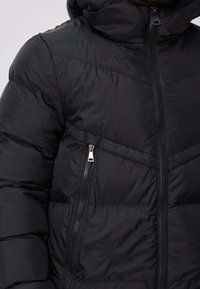 Doudoune noire à col montant, poches zippées et motif motif chevron cousu. Fabriquée en tissu lisse et léger.