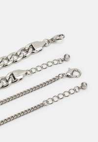 Correntes de metal prateado com elos variados; inclui um fecho tipo lagosta, detalhes em forma de esfera redonda e superfícies lisas e polidas.