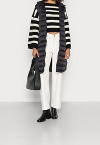 Czarna pikowana długa kamizelka na czarno-białym paskowanym krótkim swetrze, zestawiona z białymi spodniami o szerokich nogawkach i czarnymi botkami na obcasie. Czarna torebka.