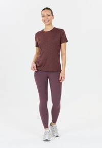 Vinröd t-shirt med kort ärm kombinerad med åtsittande lavendelfärgade leggings. Modellen bär ljusgrå sportskor. Enkla, släta tygtexturer.