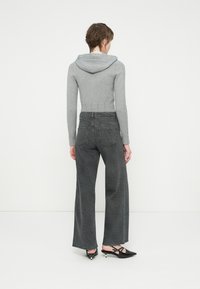 Sudadera gris ajustada con mangas texturizadas, combinada con jeans oscuros de talle alto y pierna ancha, con un acabado estampado. Zapatos básicos negros.