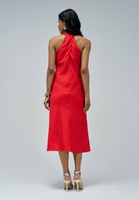 Vestido rojo de cuello halter hecho de una tela suave, con un diseño hasta la rodilla y un corsé ajustado. Se lleva con sandalias de tacón alto con tiras.