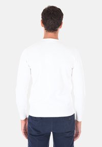 Maglione bianco a maniche lunghe in maglia con polsini e orlo a coste. Design slim fit, visto da dietro, abbinato a pantaloni blu scuro.