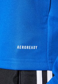 Blå sportstrøje med struktureret stof, der har "AEROREADY" logoet i hvidt. Detaljer inkluderer sort stof og kontrasterende hvide striber.