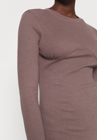 Rippiertes langärmliges Oberteil in Mauve, das ein tailliertes Design mit einem runden Halsausschnitt und Raffungen an der Brust aufweist. Weicher, strukturierter Stoff.