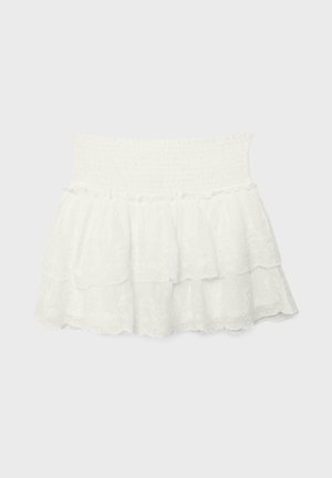 Mini-jupe blanche à volants avec taille élastique smockée et délicats détails en dentelle superposée.
