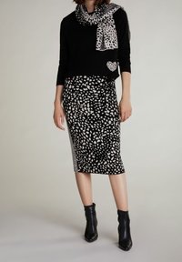 Schwarzer Pullover mit einem Herzpatch, kombiniert mit einem schwarz-weiß gefleckten Rock mit einem gemusterten Seitenstreifen. Accessoires mit einem gefleckten Schal.