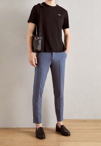 Svart bomullströja, skräddarsydda blå byxor och svarta läder loafers. Inkluderar en liten axelväska och har en enkel logotyp på tröjan.