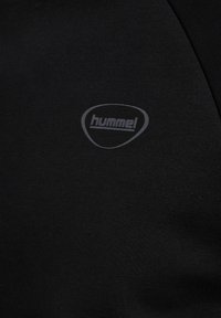 Svart bomullströja med en subtil, strukturerad logotyp i grått av varumärket "hummel" på övre vänstra sidan. Enkla, figursydd design.