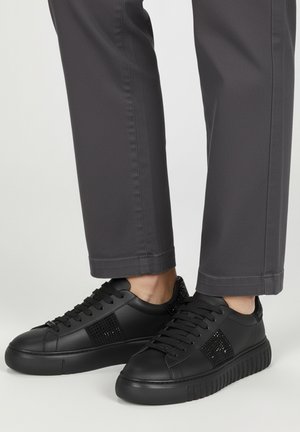 Zwarte sneakers met een glad leren afwerking, voorzien van mesh panelen en dikke rubberen zolen. Vetersluiting met tonale stiksels en minimalistische branding.