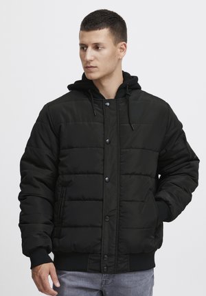 Sort pufferjakke med polstret design, trykknaplukning og sidelommer. Har hætte og ribbede manchetter for ekstra varme.