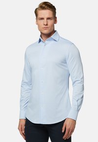 Svetlomodrá košeľa s dlhým rukávom vyrobená z hladkého materiálu, s ostrým golierom a bielymi gombíkmi na prednej strane. Elegantný strih.