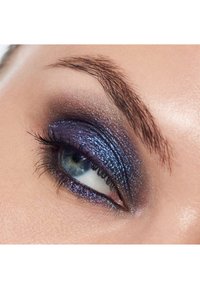 Nahaufnahme eines Auges mit blau-grünem Iris und schimmerndem metallischem Blau und lila Lidschatten, der in einen rauchigen Look übergeht, umrahmt von natürlichen Wimpern.