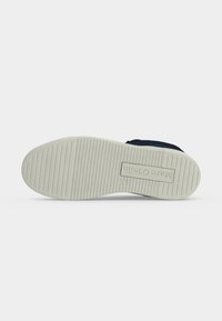 Semelle en caoutchouc blanche d'une chaussure bleu marine avec des rainures horizontales et « Marc O’Polo » embossé près du talon.