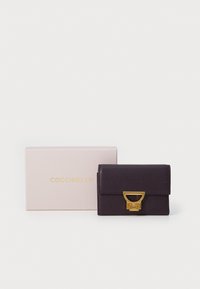 Plum leather wallet with a smooth texture, featuring a gold-tone hardware clasp. Accompanied by a light pink box displaying 'Coccinelle' logo.
