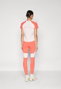 Athletic outfit featuring a coral and white short-sleeve top with color-blocked leggings. Made of stretchy fabric with minimal stitching details.