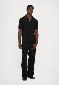Sort polo skjorte med krage og hvit søm, kombinert med løstsittende svarte bukser og svarte sko. Enkel design, uten mønster.