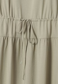 Robe en tissu beige avec une taille froncée, dotée d'un détail cordon noué au centre devant.