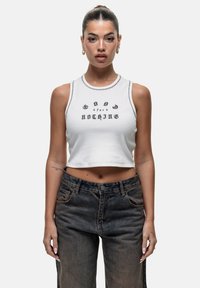 Biała krótka bluzka na ramiączkach z czarnym napisem, zestawiona z ciemnoniebieskimi dżinsami z wysokim stanem. Koszulka ma kontrastowe szwy i prążkowany dekolt.