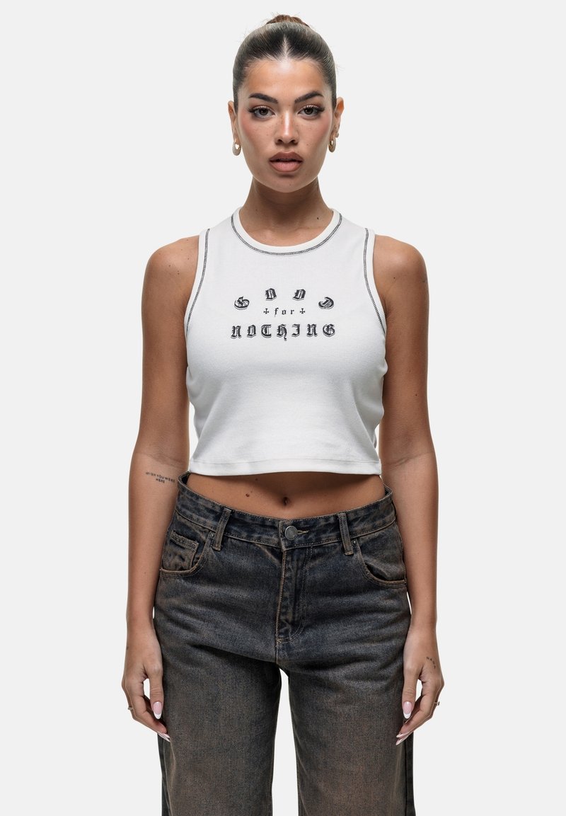 Biała krótka bluzka na ramiączkach z czarnym napisem, zestawiona z ciemnoniebieskimi dżinsami z wysokim stanem. Koszulka ma kontrastowe szwy i prążkowany dekolt.