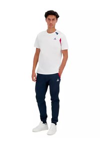 Camiseta blanca de manga corta con detalles en azul y rojo, combinada con joggers azul marino. Tejido texturizado, diseño ajustado, logotipo en el pecho.