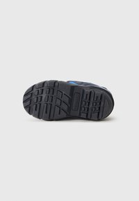 Suela de goma negra de una bota de invierno azul que muestra surcos profundos y el nombre de la marca "Sorel" estampado en el centro.