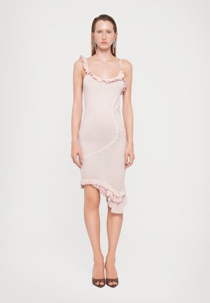 Vestido ajustado de un rosa claro con un escote con volantes y dobladillo asimétrico. Textura suave y tirantes finos, combinado con tacones abiertos de color marrón.