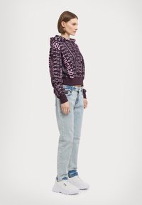 Felpa viola con testo grafico rosa a contrasto, design cropped, orlo a coste, abbinata a jeans dritti blu chiaro e sneakers bianche.