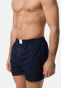 Donkerblauwe katoenen boxershorts met een elastische tailleband, voorzien van rode knopen aan de voorkant. Soepele textuur, ontspannen pasvorm.