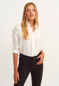 Weißes Hemd mit Kragen, hochgekrempelten Ärmeln, kombiniert mit hochgeschnittenen schwarzen Jeans. Glatte Textur, minimalistisches Design.