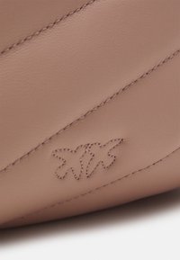 Lichtroze leren tas met diagonale gestructureerde stiksels en een subtiel geborduurd logo aan de zijkant, met zowel gladde als matte afwerkingen.