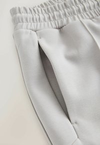 Light gray sweatpants featuring a textured elastic waistband, side pockets with a smooth finish, and tapered leg design.