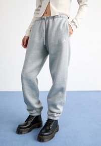 Graue Fleece-Jogginghosen mit elastischem Bund und Kordelzug, ausgestattet mit seitlichen Taschen. Kombiniert mit schwarzen klobigen Schnürstiefeln mit gelben Nähten.