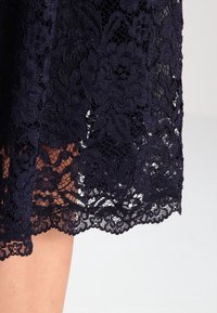 Jupe en dentelle navy avec des motifs floraux, des détails intricats et un ourlet festonné, avec une texture douce et des sections semi-transparentes.
