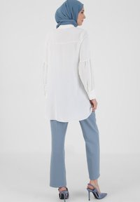 White long-sleeve blouse with puffed sleeves, high-low hem; paired with light blue straight-leg pants and blue high-heeled shoes.
