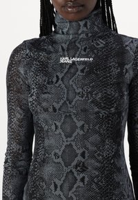 Juoda ir pilka gyvatės rašto ilgomis rankovėmis palaidinė su aukštu kaklu, pagaminta iš elastingos medžiagos. Savybėje - balta "KARL LAGERFELD JEANS" logo.