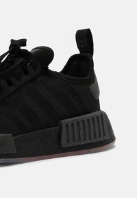 Scarpa sportiva nera con tomaia in mesh testurizzato, tre strisce distintive e suola in gomma rigata. Dotata di un lembo di presa sul tallone.