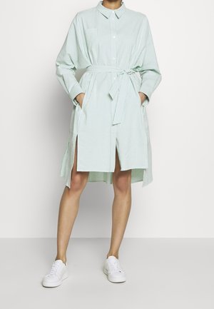 Light green striped shirt dress with a collar, long sleeves, side slits, and a tied waist. Styled with white sneakers.