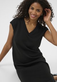 Robe noire à col en V avec manches courtes, texture lisse et coupe décontractée, portée par un mannequin sur un fond uni.