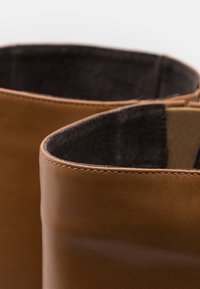 Brązowe skórzane botki za kostkę o gładkiej fakturze, zaokrąglonych czubkach, kontrastującym ciemnym wnętrzu i precyzyjnych detalach przeszycia.