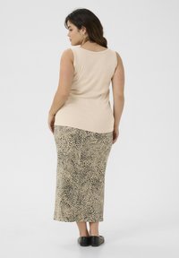Beige ärmelloses Top kombiniert mit einem langen, leopardbedruckten Rock in Beige und Schwarz. Der Stoff scheint glatt und enganliegend zu sein. Schwarze flache Schuhe.