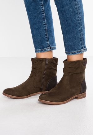 Bottines en daim marron avec une fermeture éclair latérale, une semelle marron clair et des accents texturés noirs au niveau du talon. Le design présente un revers plié.